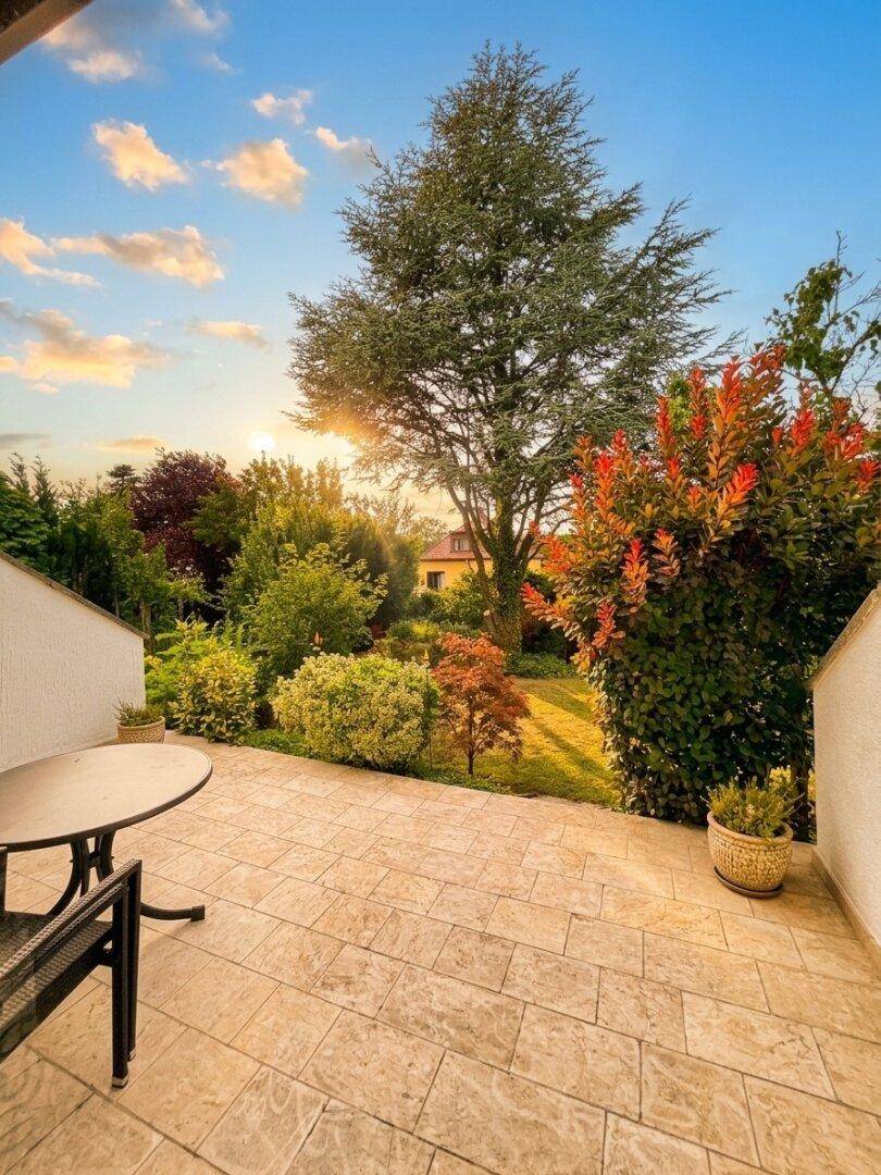 Sonniger Terrassenbereich mit Gartenmöbeln und Blick auf den grünen Garten bei Sonnenuntergang.