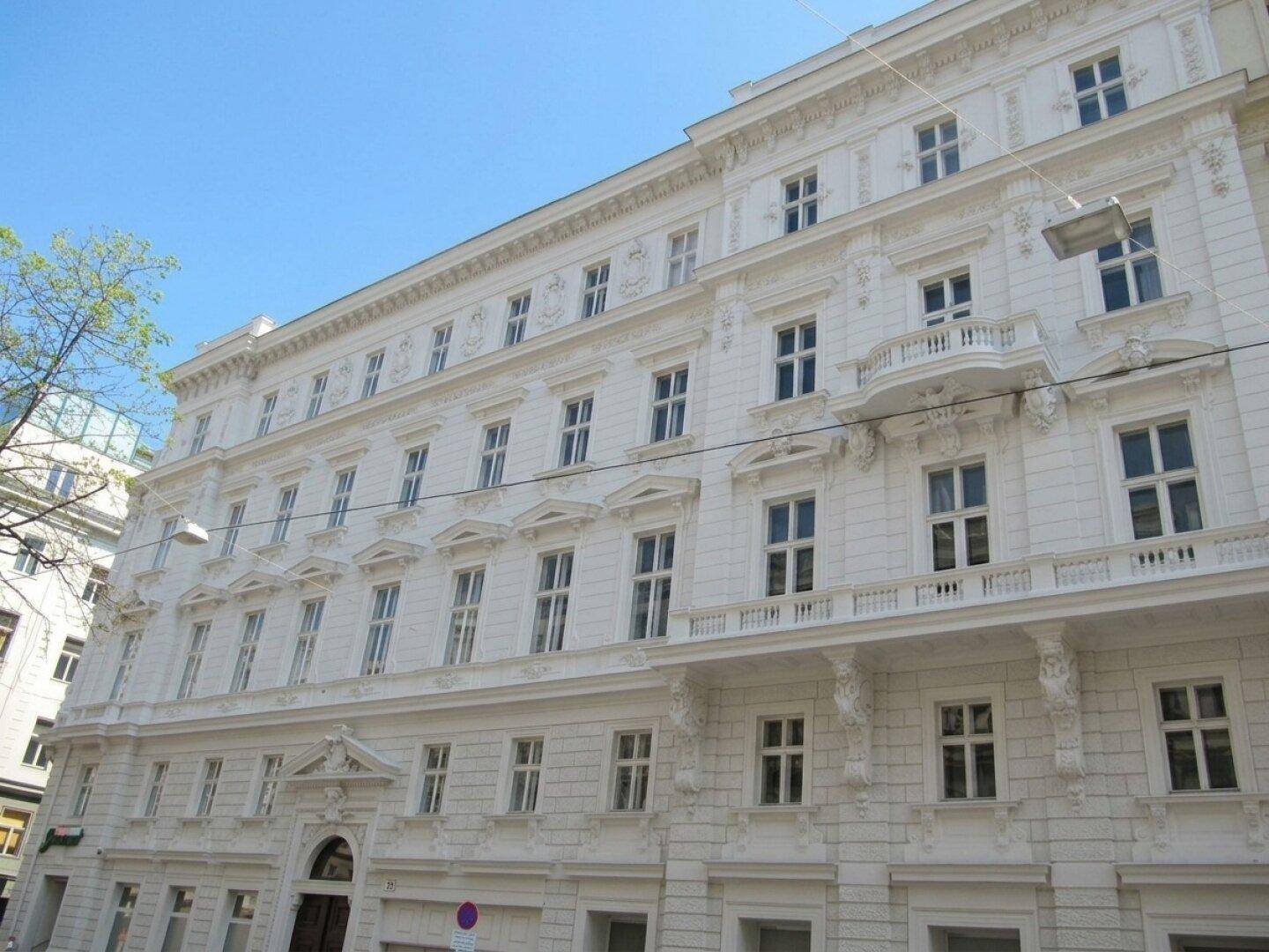 Elegantes Altbaugebäude mit weißer Fassade, reich verzierten Details und mehreren Balkonen.