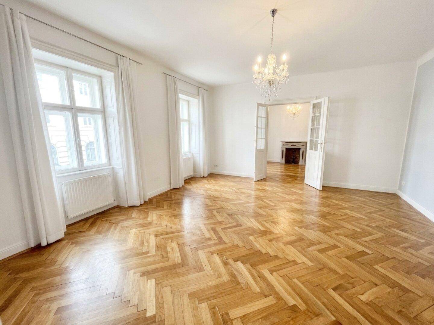 Helles Wohnzimmer mit klassischem Fischgrätparkett und Blick auf einen eleganten Kamin im angrenzenden Raum.