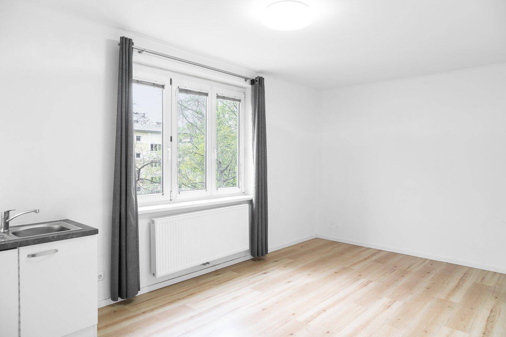 Heller, leerer Raum mit großen Fenstern, hellem Holzboden und weiß gestrichenen Wänden, ideal für individuelle Gestaltung.
