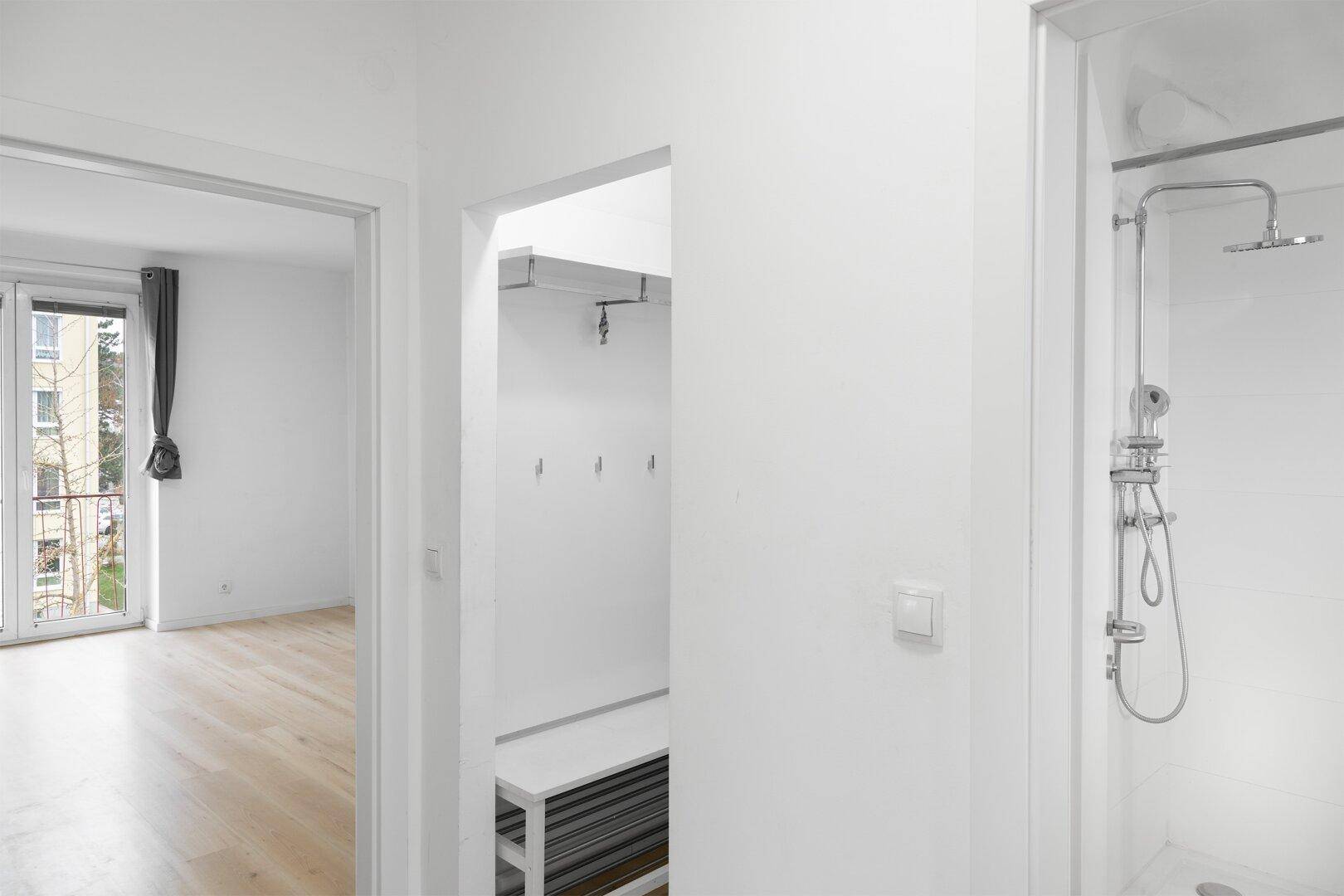Blick von einem Raum mit Balkonzugang in einen Flurbereich mit Garderobe und angrenzender Dusche.