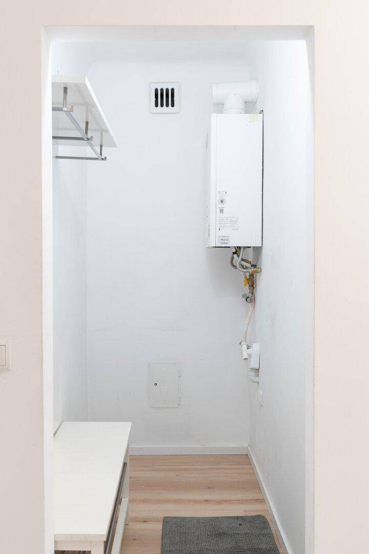 Kleiner Hauswirtschaftsraum mit Warmwasserbereiter, Lüftung und praktischer Ablagefläche.