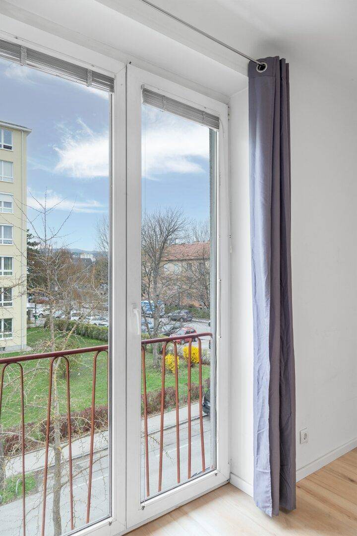 Große Balkontür mit rotem Geländer, die den Blick auf die Straße und umliegende Gebäude freigibt.
