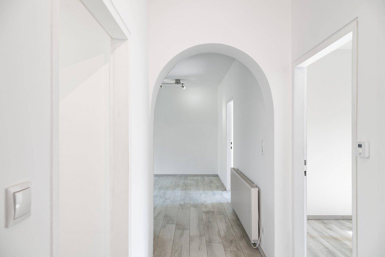 Heller Flur mit elegantem Bogen, modernem Laminatboden und weiß gestrichenen Wänden.
