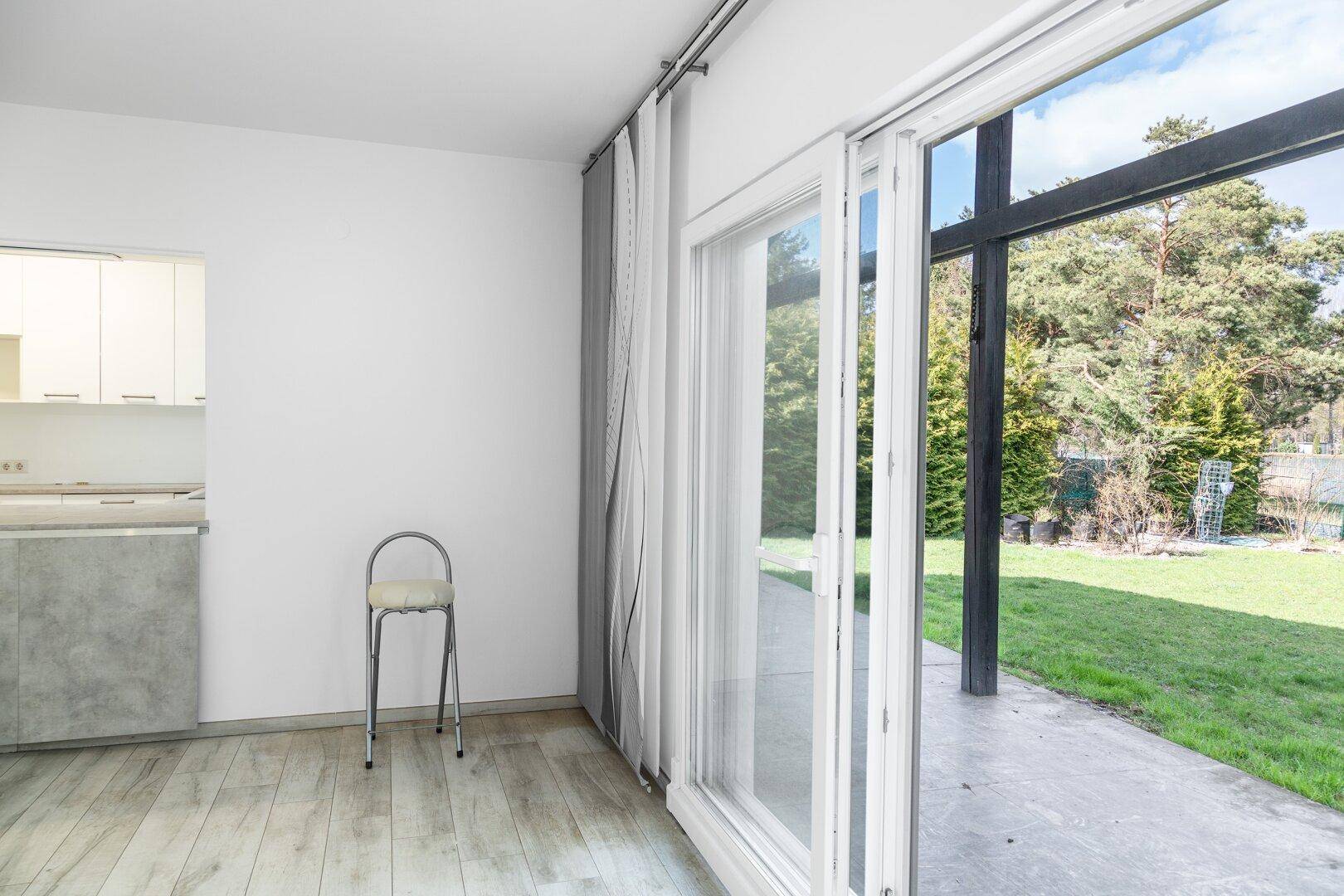 Wohnbereich mit Blick in die Küche und Zugang zum Garten durch große Schiebetüren.