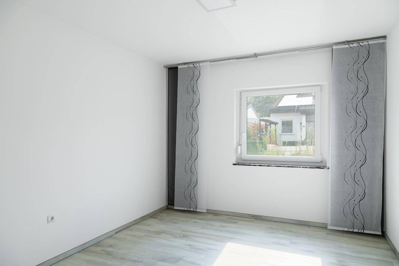 Geräumiges Zimmer mit Laminatboden, Fenster und dekorativen Vorhängen.