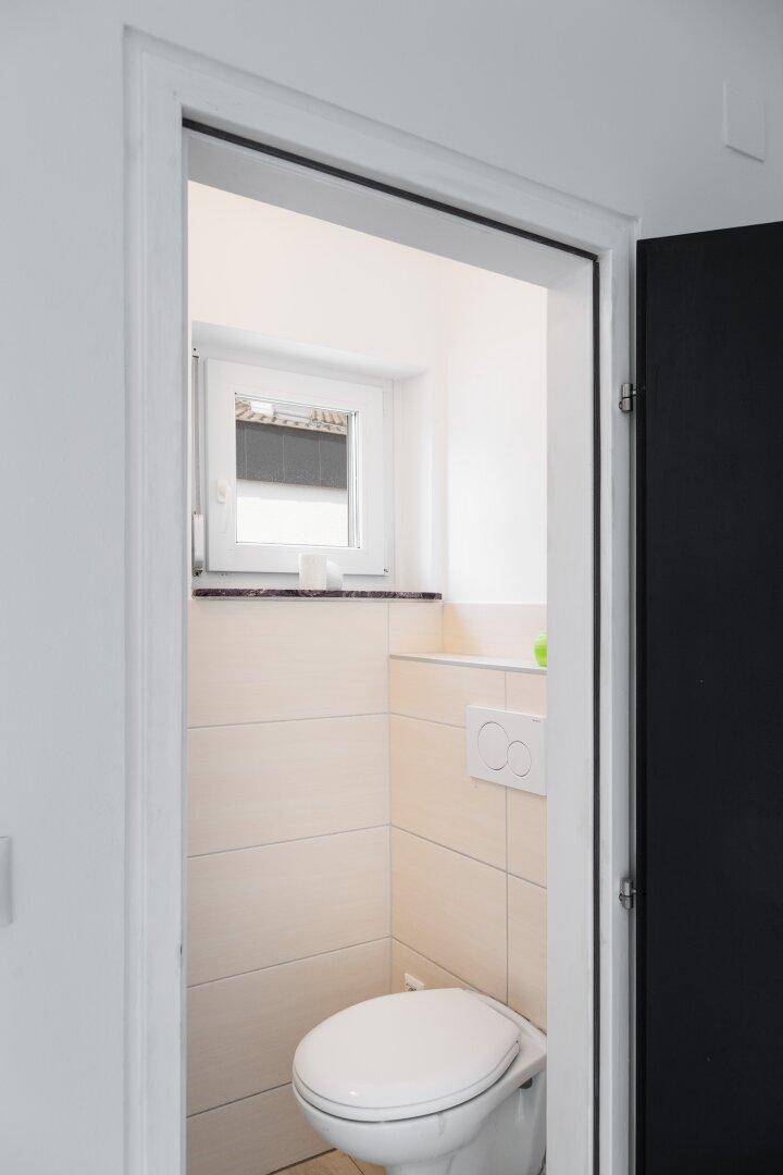 Kleines Gäste-WC mit Fenster, Wand-WC und hellen Fliesen.