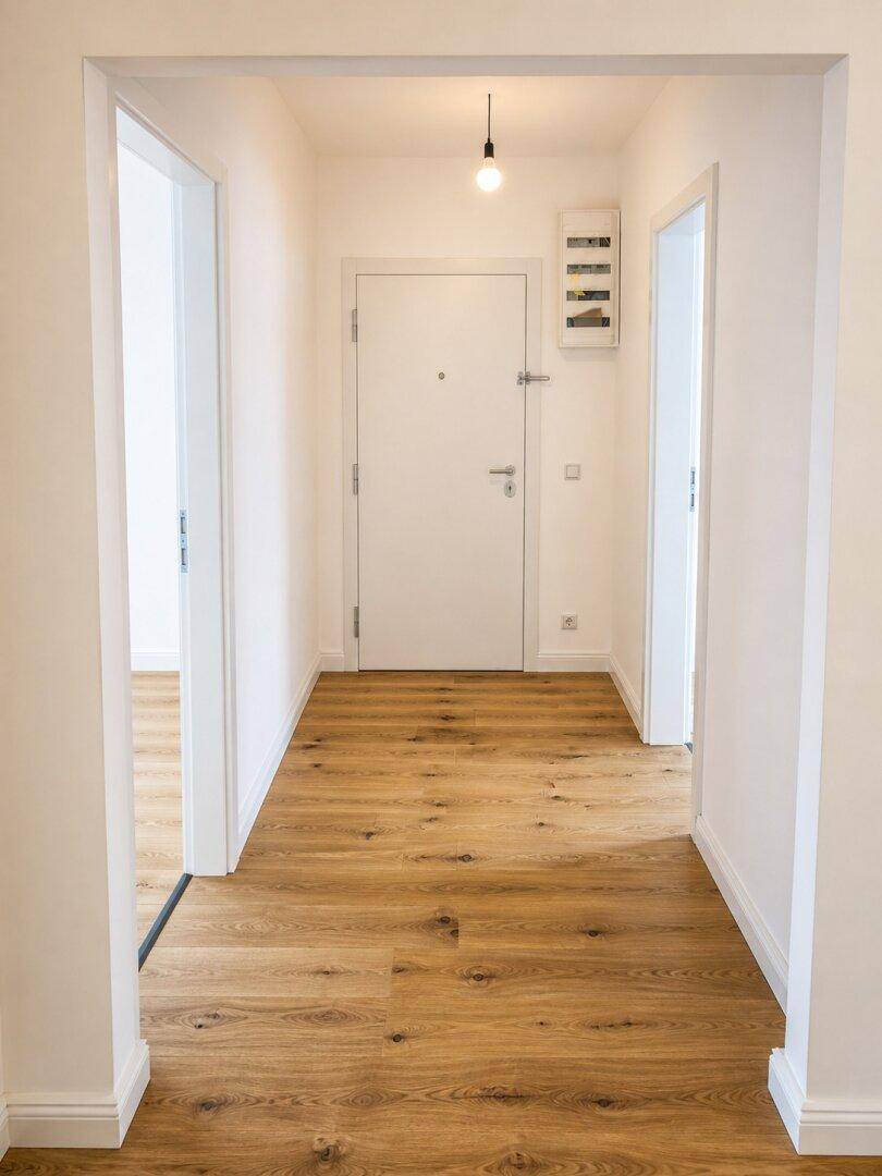 Heller Flur mit Holzboden, weißer Eingangstür und Zugang zu weiteren Räumen.