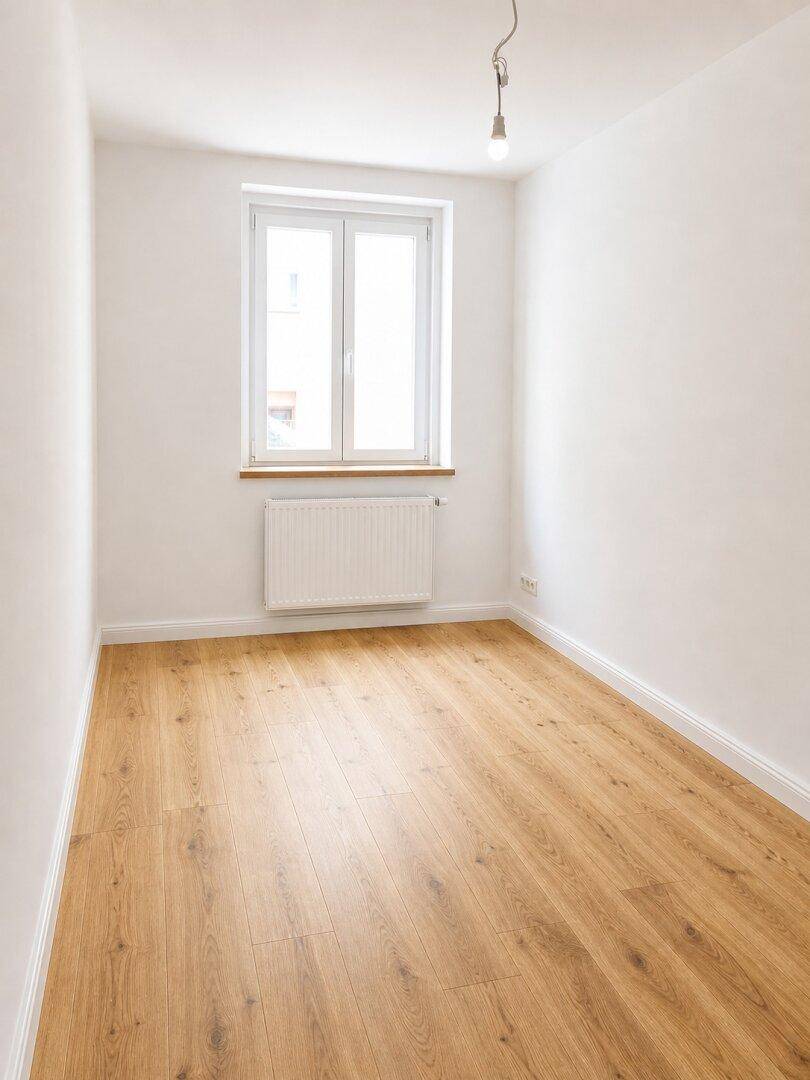 Kleiner, heller Raum mit einem Fenster, Holzboden und weiß gestrichenen Wänden.