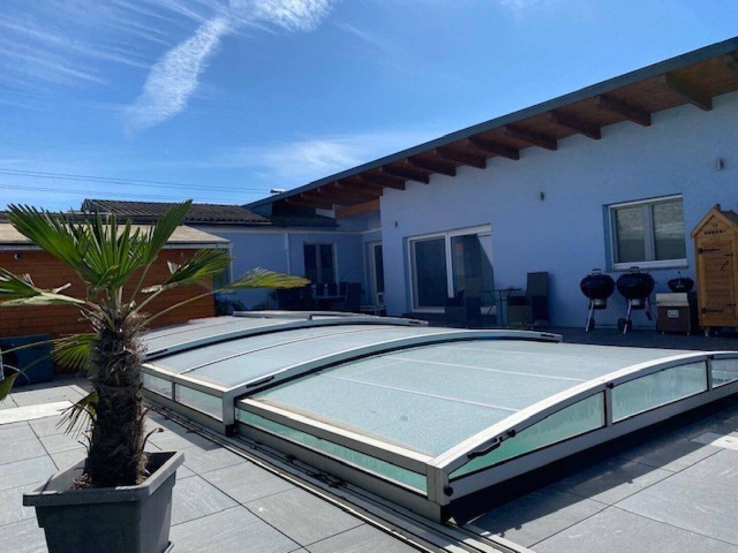 Überdachter Swimmingpool im Außenbereich des Hauses mit blauer Fassade und Palmen.