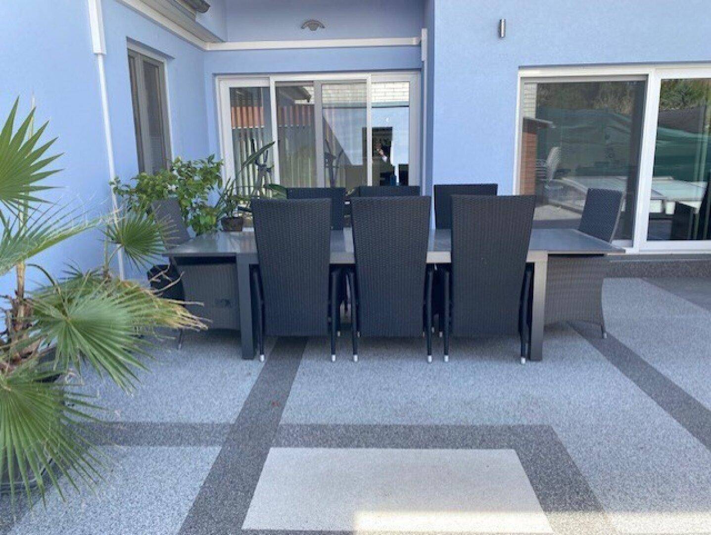 Möblierte Terrasse mit großem Esstisch und Stühlen vor der blauen Hausfassade.