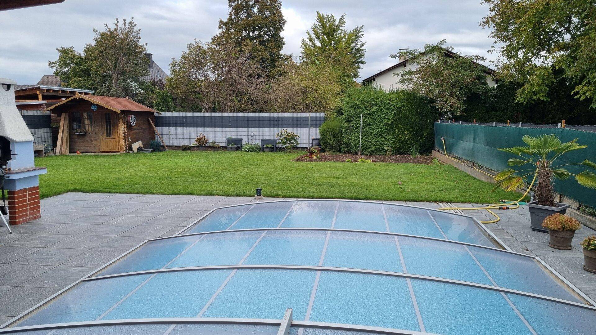 Gepflegter Garten mit Rasenfläche, überdachtem Pool und einem Gartenhaus.