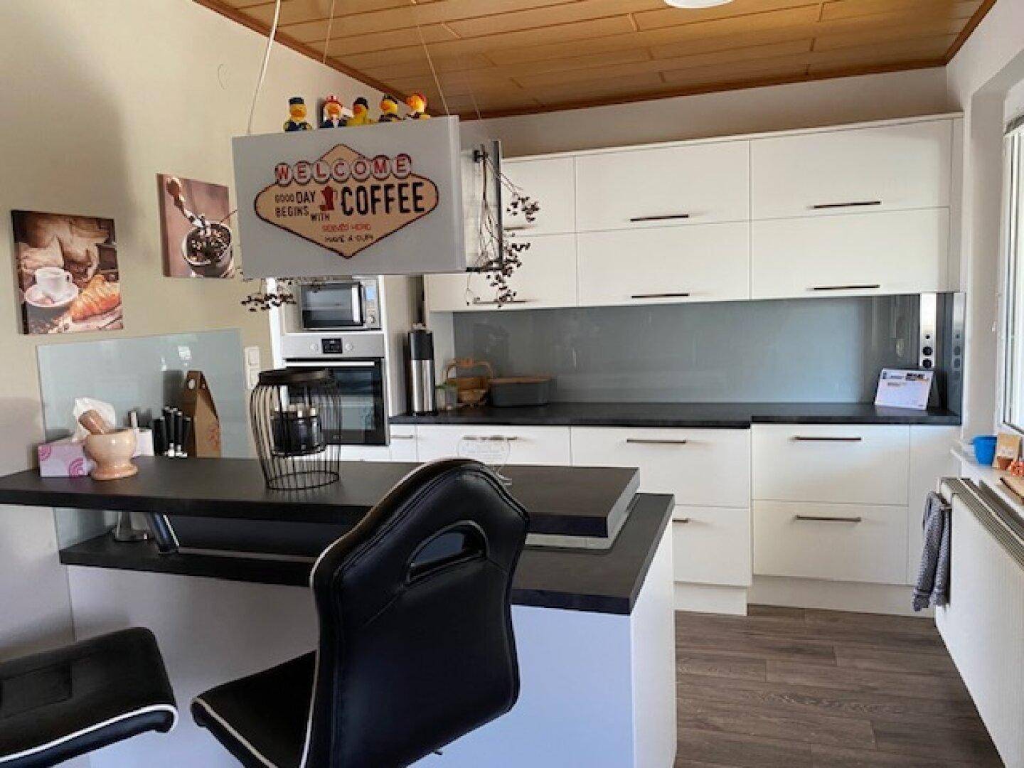 Moderne Küche mit weißen Schränken, dunklen Arbeitsplatten und Frühstücksbar.
