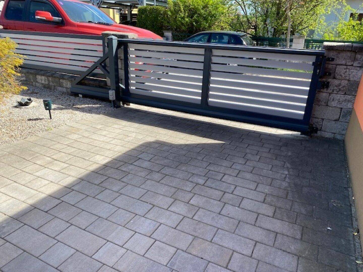 Moderner Eingangsbereich mit Schiebetor und gepflasterter Auffahrt.