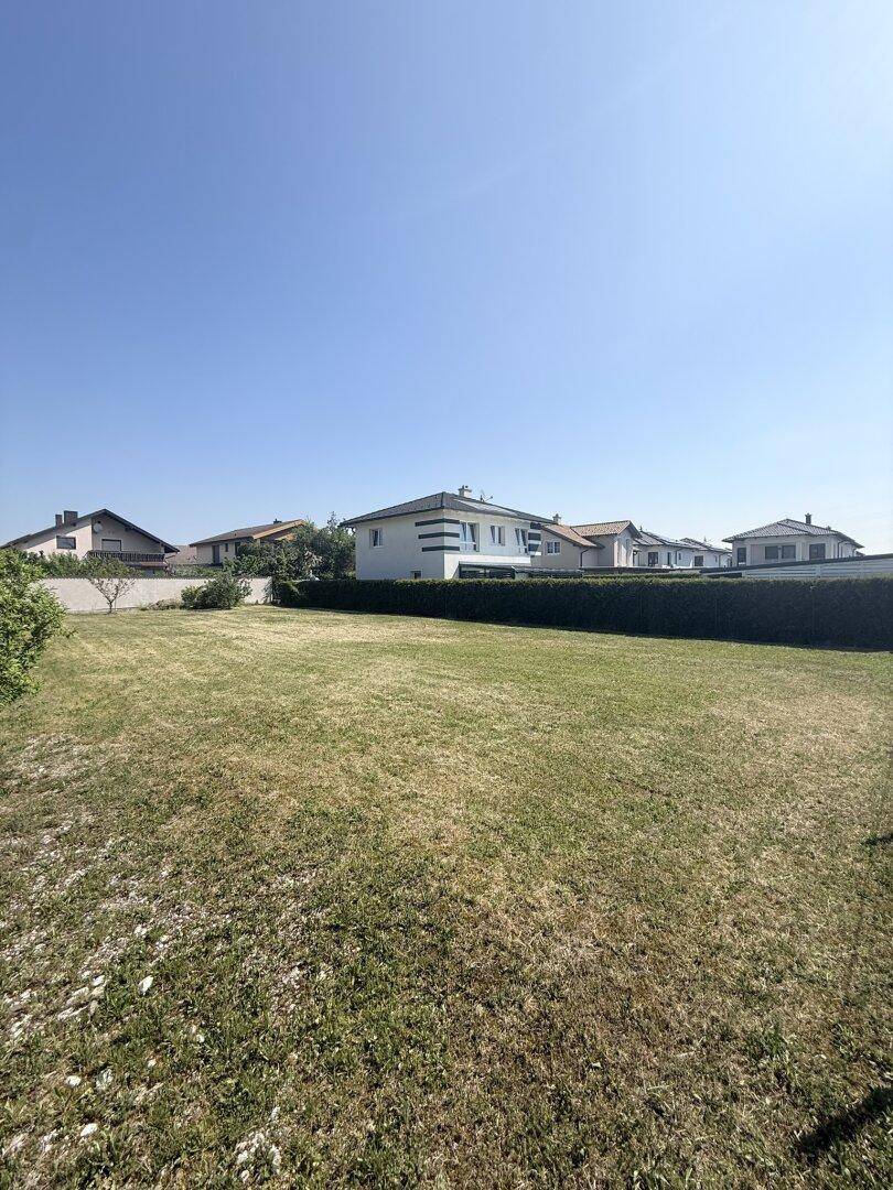 Offenes Gartengrundstück mit Rasenfläche und Blick auf eine Reihe von Wohnhäusern in der Ferne.