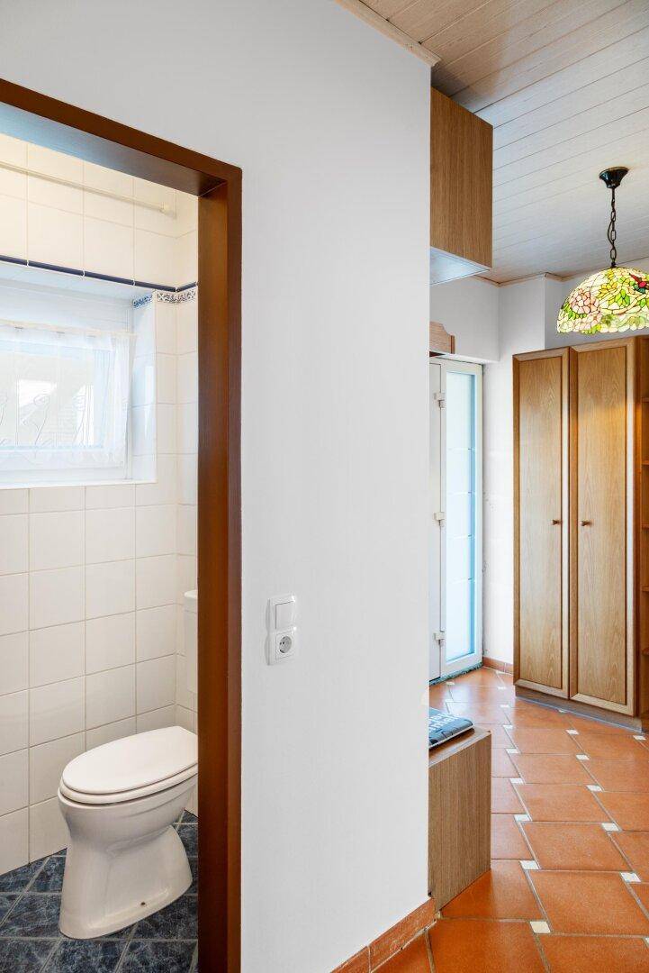 Kleines Gäste-WC mit Fenster, weißen Fliesen und dunklem Boden.