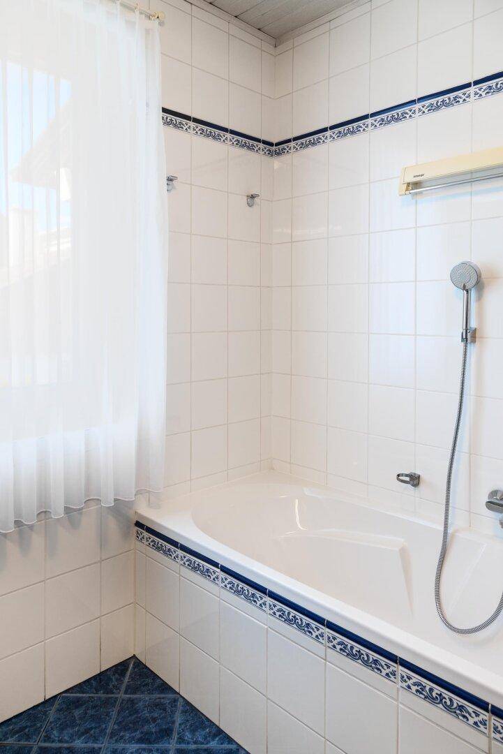 Badezimmer mit Badewanne, weißen Fliesen und Fenster für natürliches Licht.