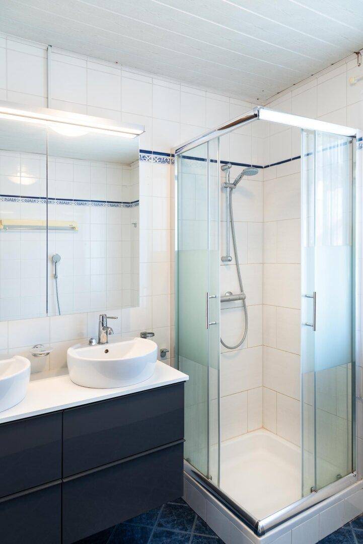 Modernisiertes Badezimmer mit Doppelwaschbecken, Duschkabine und weißen Fliesen.
