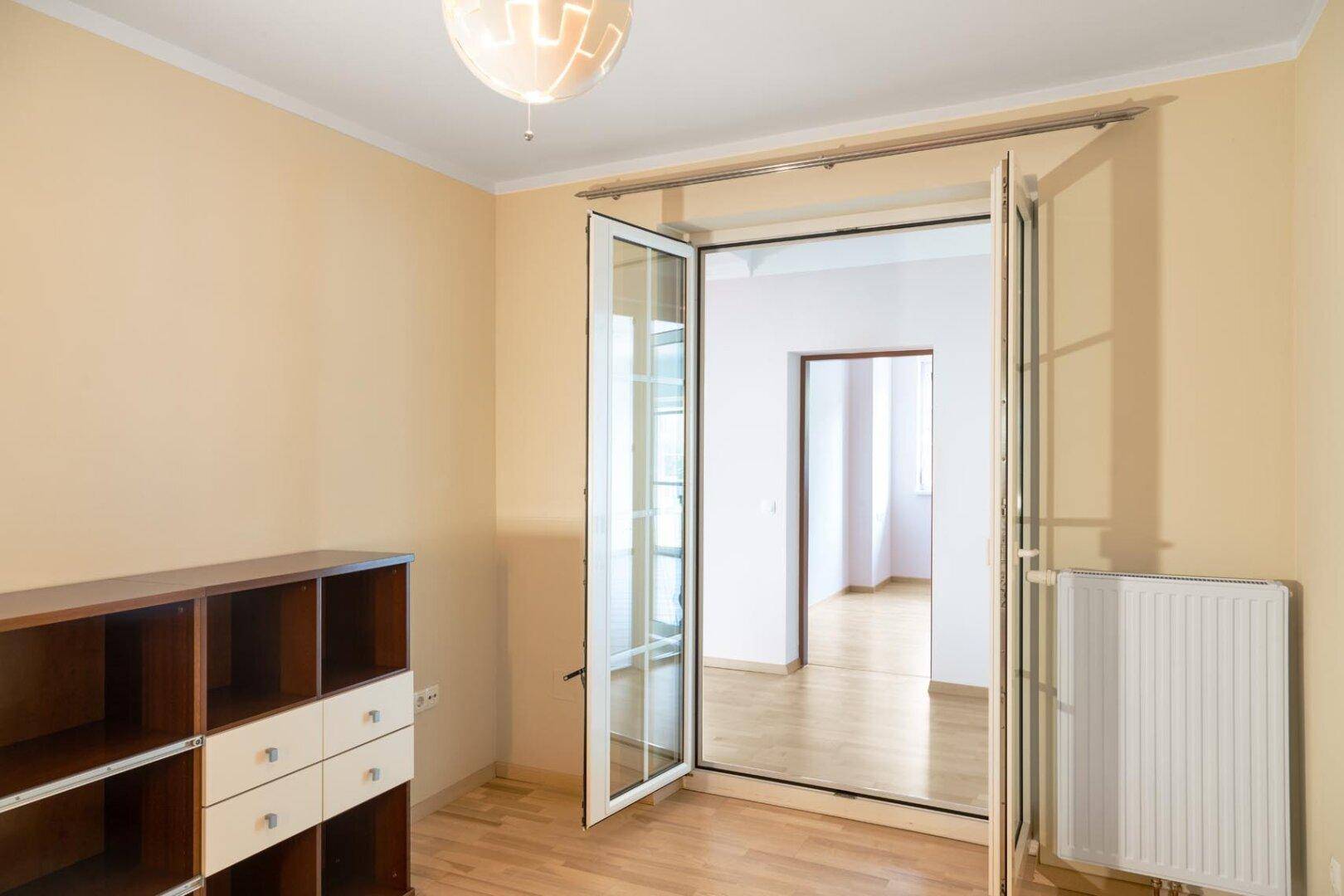 Heller Raum mit Parkettboden und Glastüren, die zu einem weiteren Zimmer führen.