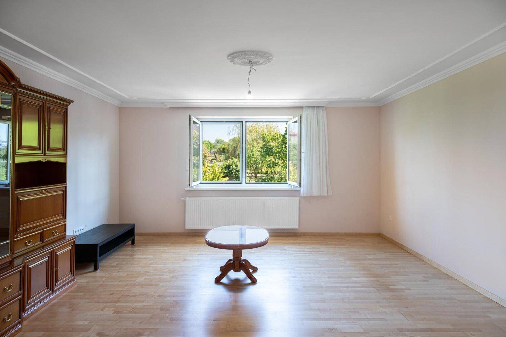 Gemütliches Wohnzimmer mit Parkettboden, Fenster und Blick in den grünen Garten.