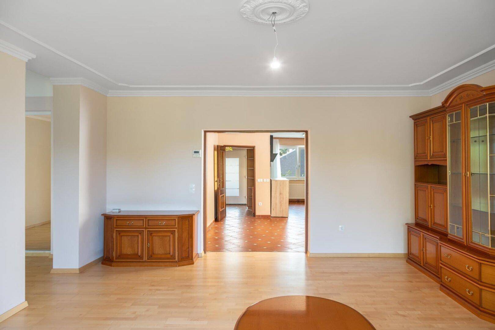 Helles Wohnzimmer mit Parkettboden, Stuckdecke und traditionellen Holzmöbeln.