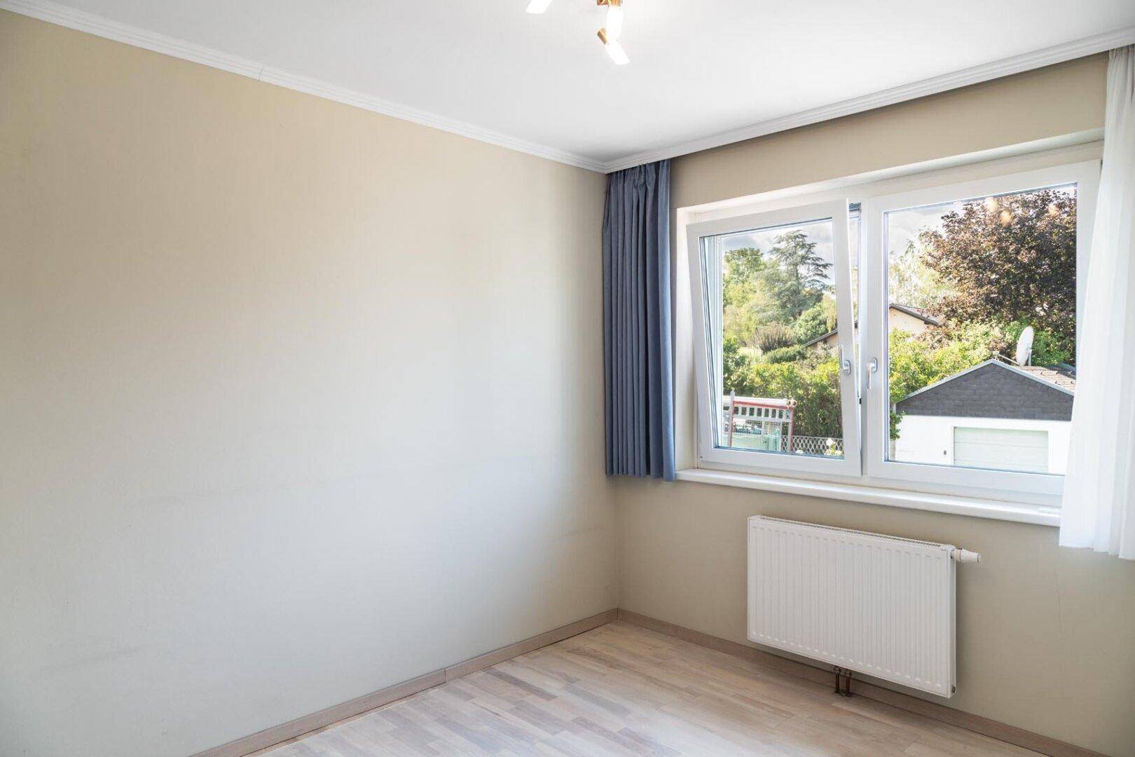 Helles Schlafzimmer mit Parkettboden, großem Fenster und Blick ins Grüne.