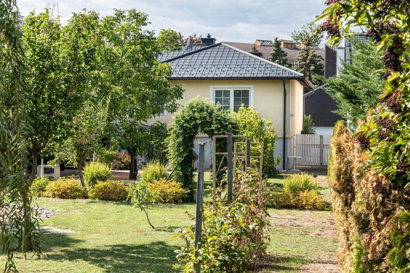 Großer, grüner Garten mit Bäumen, Sträuchern und einem Gartenbogen.