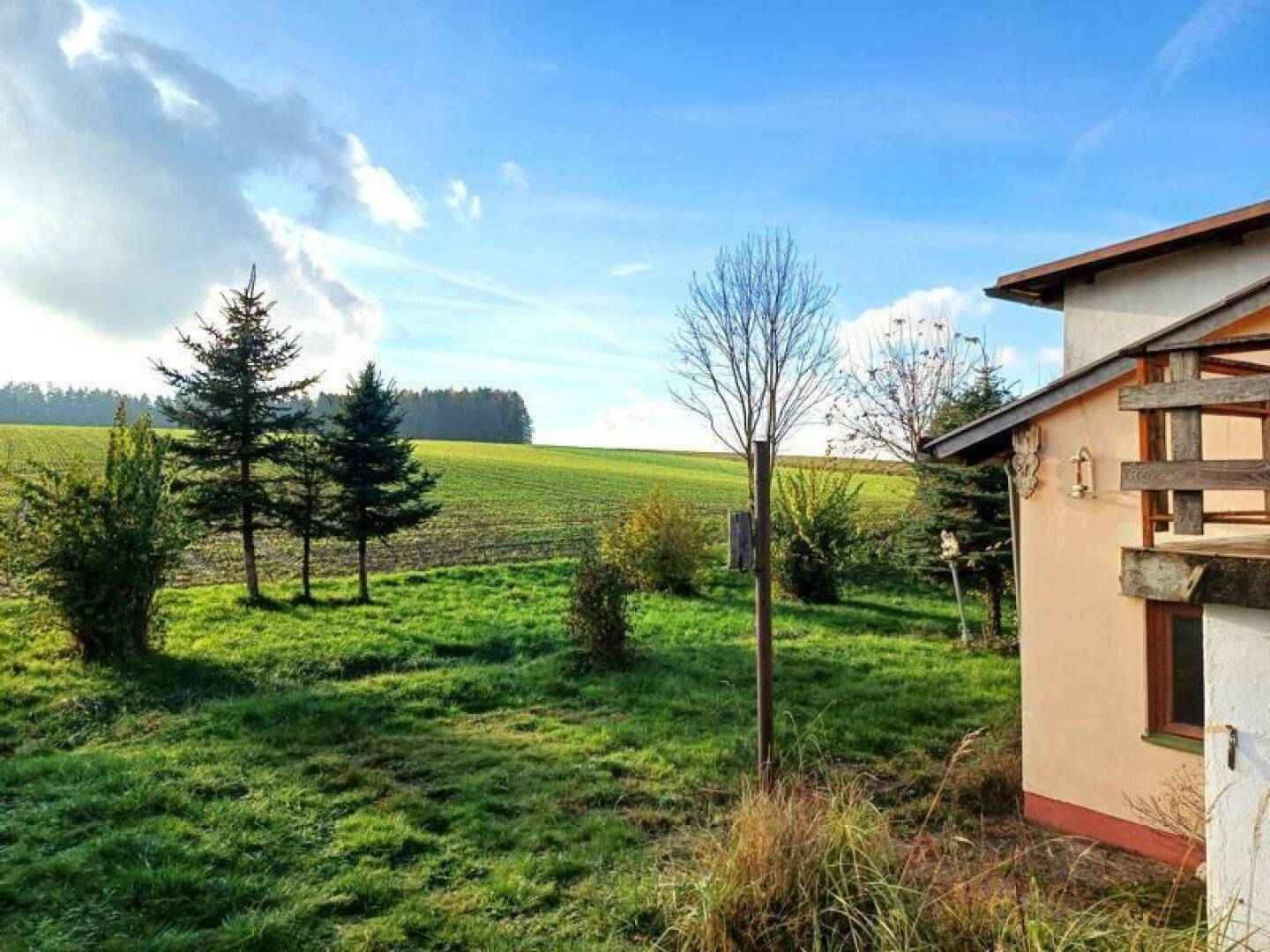 Blick auf ein Haus und weite grüne Felder, die sich bis zum Horizont erstrecken, unter blauem Himmel.