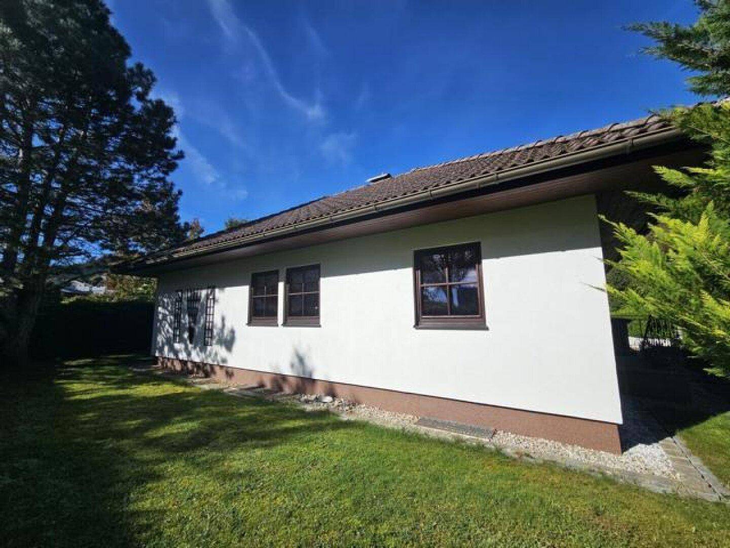 Lange Seitenansicht des Hauses mit mehreren Fenstern und einem sonnigen Rasenbereich.