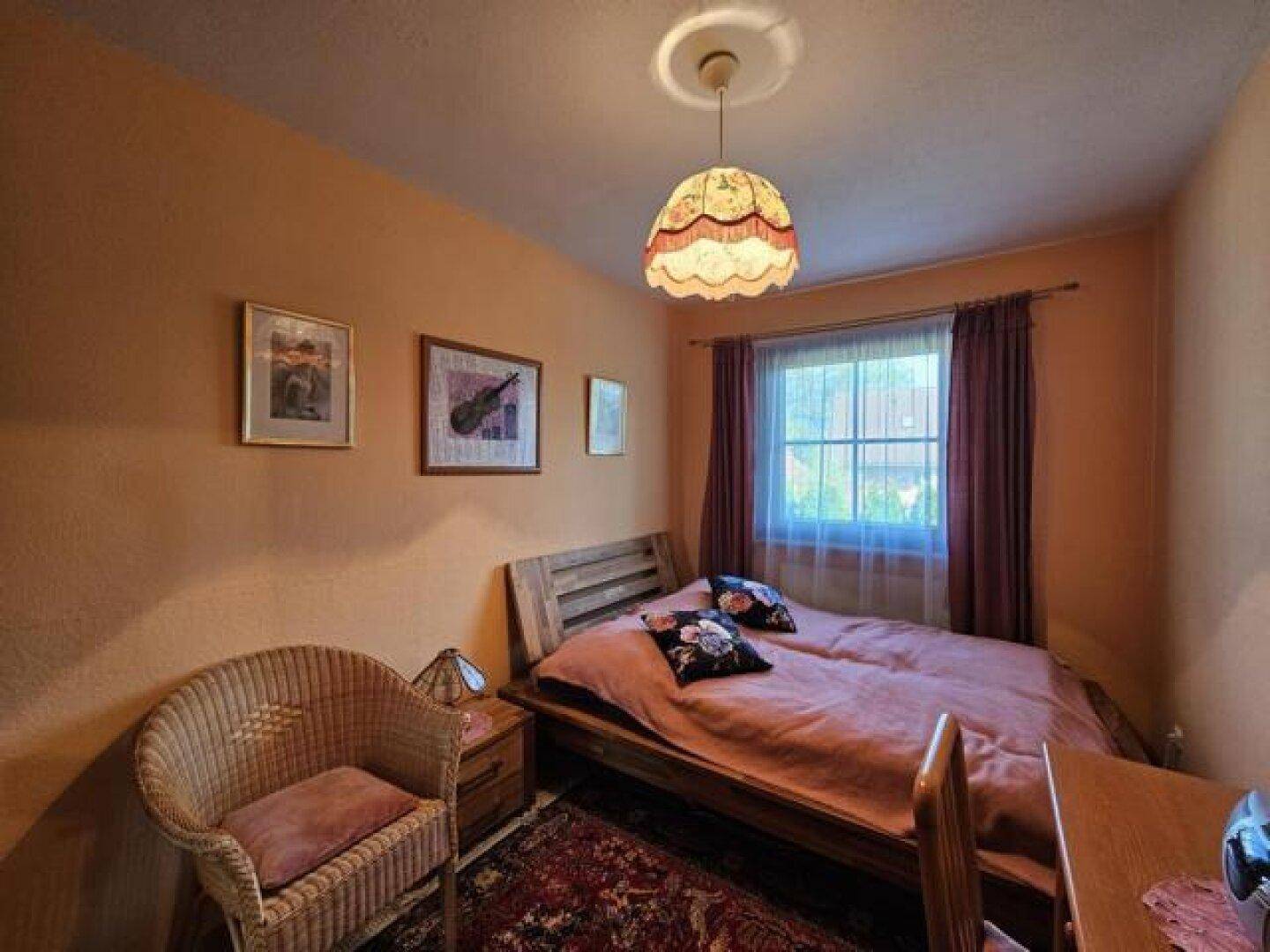 Gemütliches Schlafzimmer mit Holzbett, Korbsessel und Fenster mit Vorhängen.