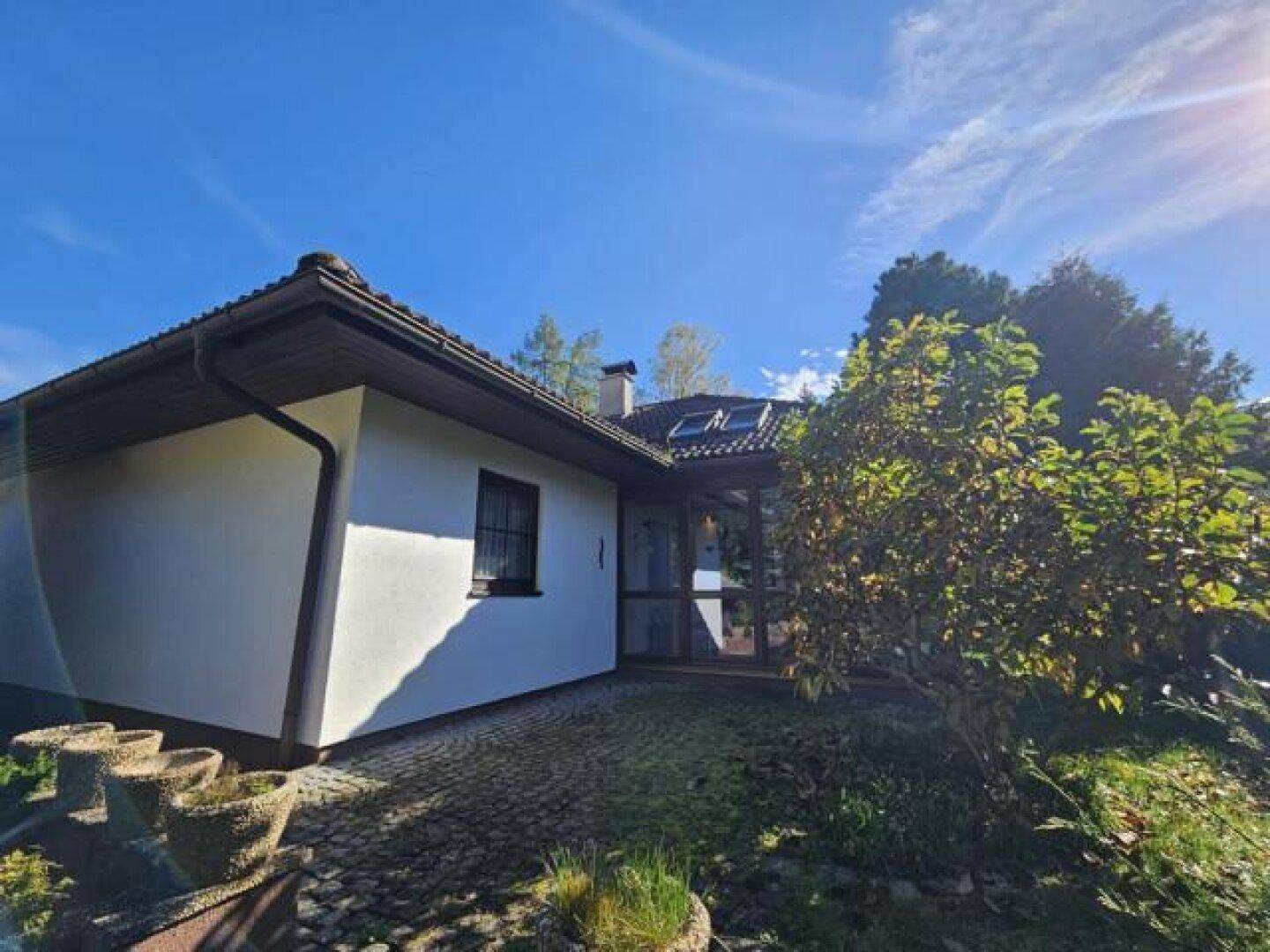 Seitenansicht des Hauses mit weißer Fassade, Wintergarten und gepflastertem Bereich.