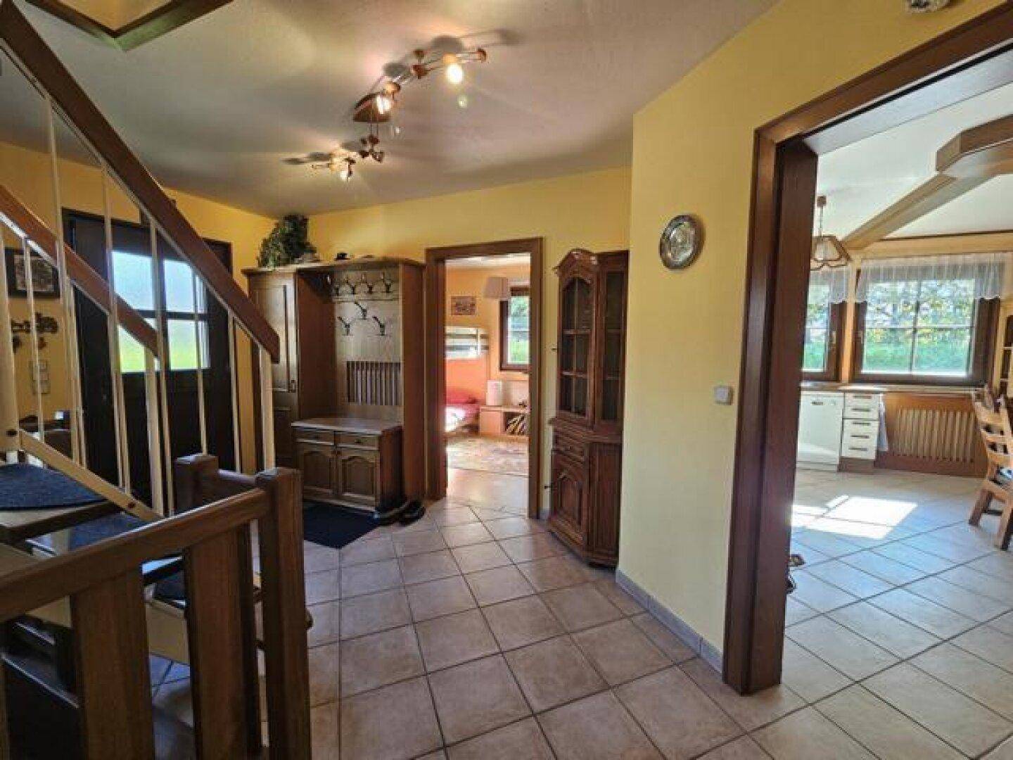 Heller Eingangsbereich mit gefliestem Boden, Holztreppe und Garderobe.