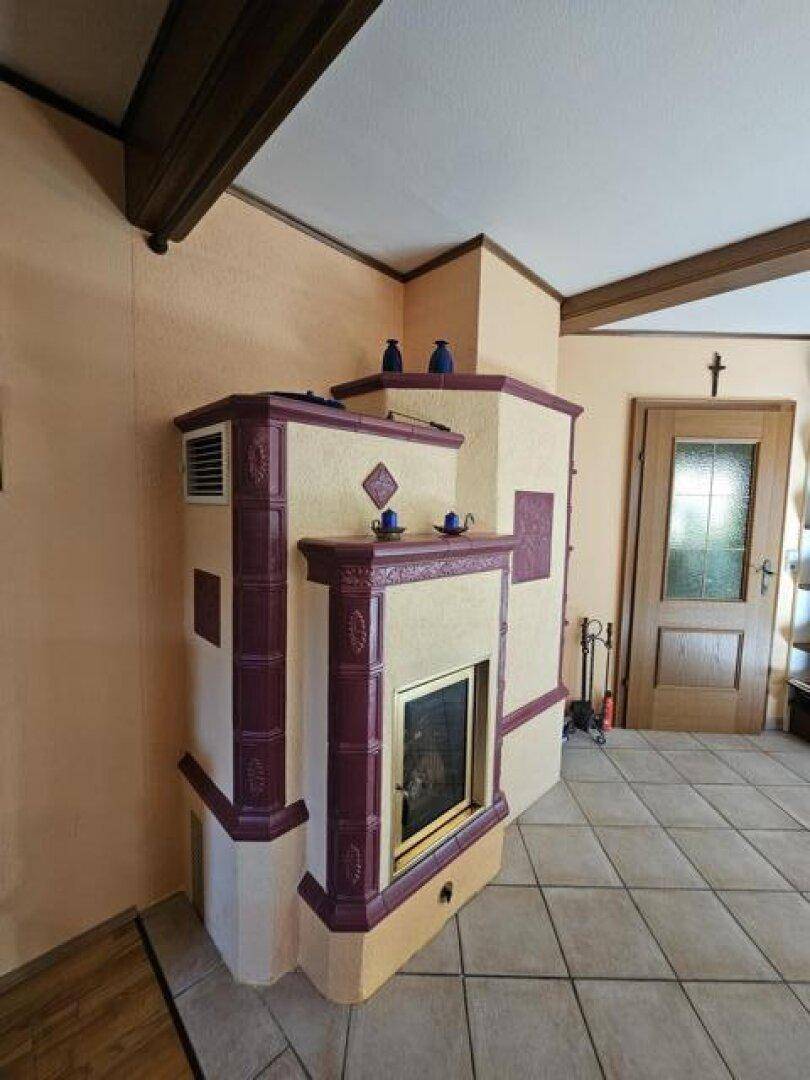 Traditioneller Kachelofen im Wohnbereich mit gefliestem Boden und Holzbalken an der Decke.