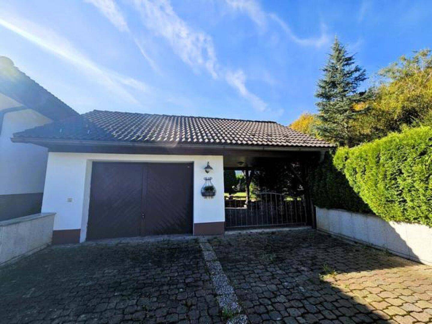 Garage mit zwei Toren und gepflasterter Zufahrt, umgeben von Grünflächen und Hecken.