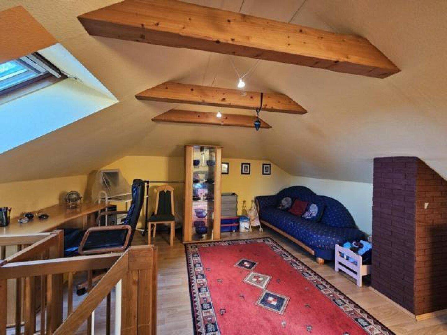 Geräumiger Dachboden mit Holzbalken, Schreibtisch und Sofa, ideal als Arbeits- oder Wohnbereich.
