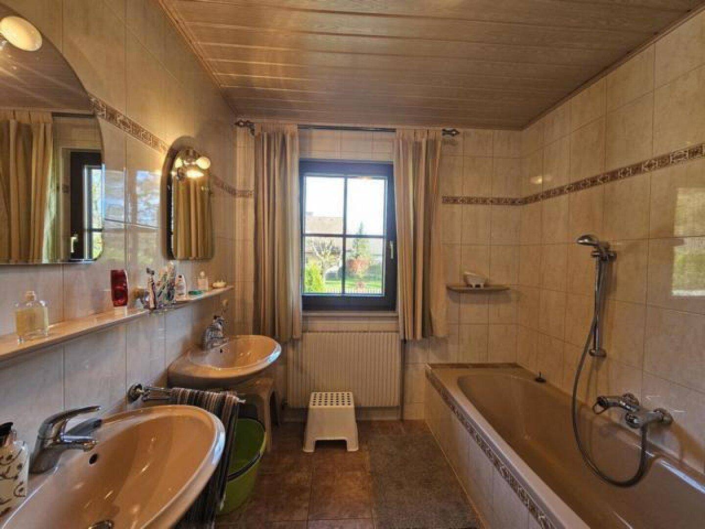 Badezimmer mit zwei Waschbecken, Badewanne und Fenster mit Blick ins Grüne.