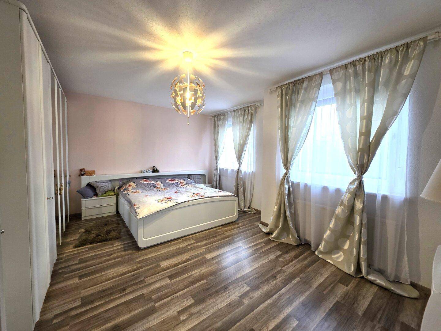 Schlafzimmer mit Doppelbett, weißen Kleiderschränken und hellem Laminatboden.