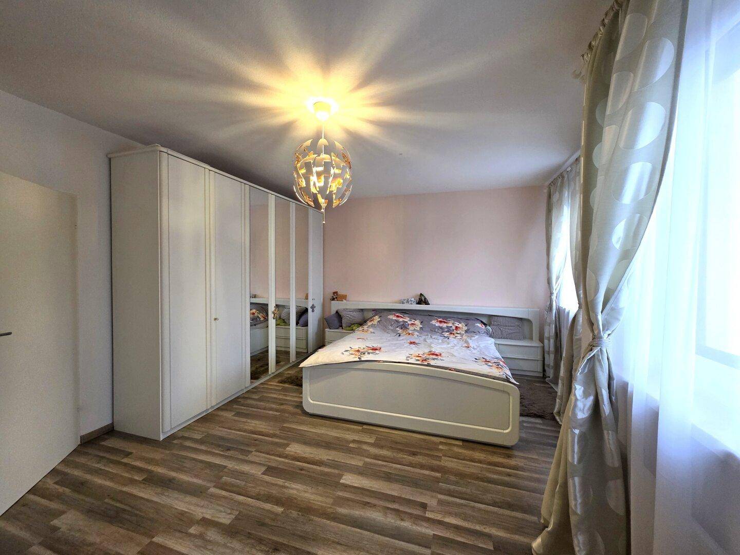 Geräumiges Schlafzimmer mit großem Bett, Spiegelschränken und hellem Laminatboden.