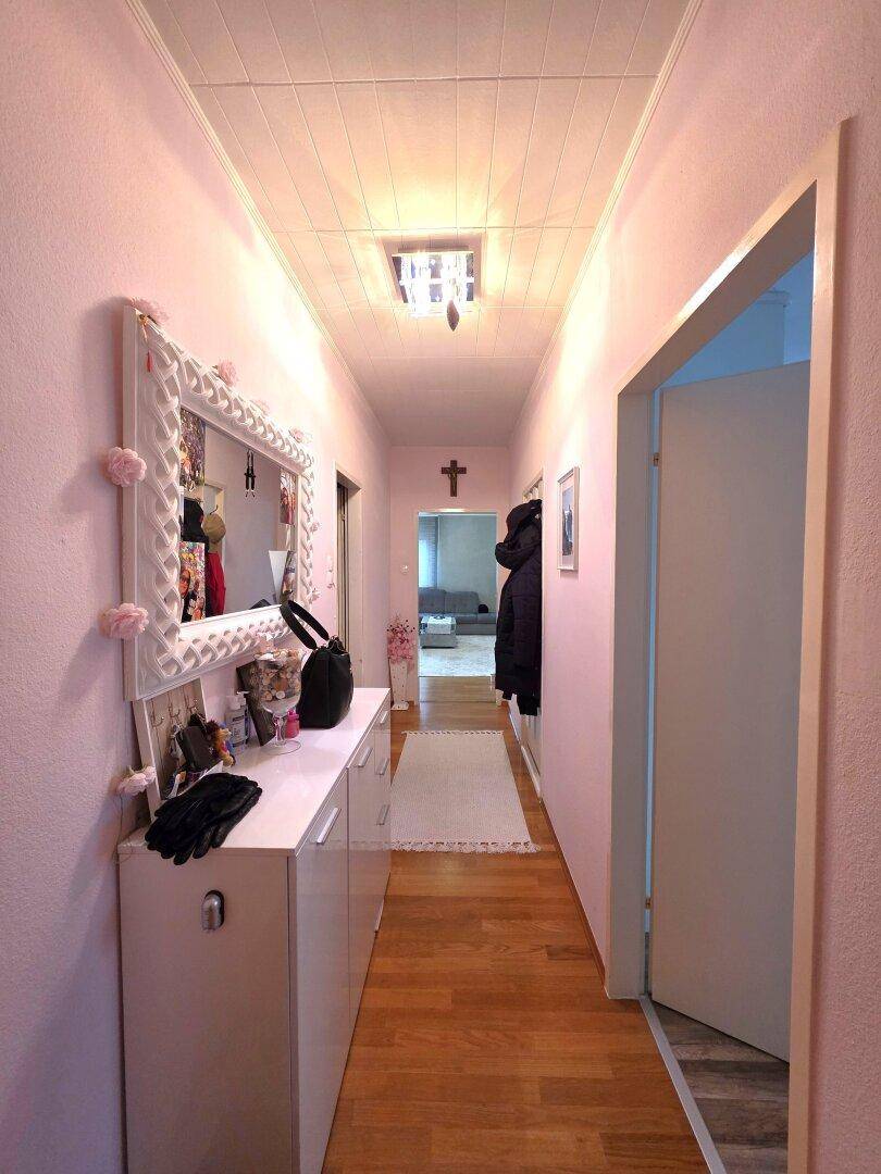 Langer Flur mit rosa Wänden, Spiegel und Holzfußboden.