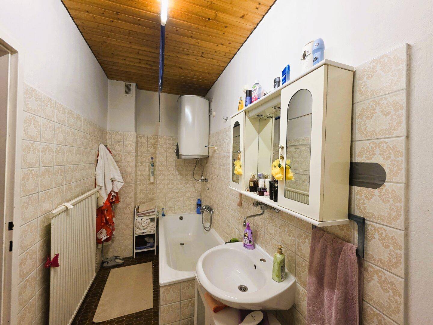 Badezimmer mit Badewanne, Waschbecken und Holzdecke.