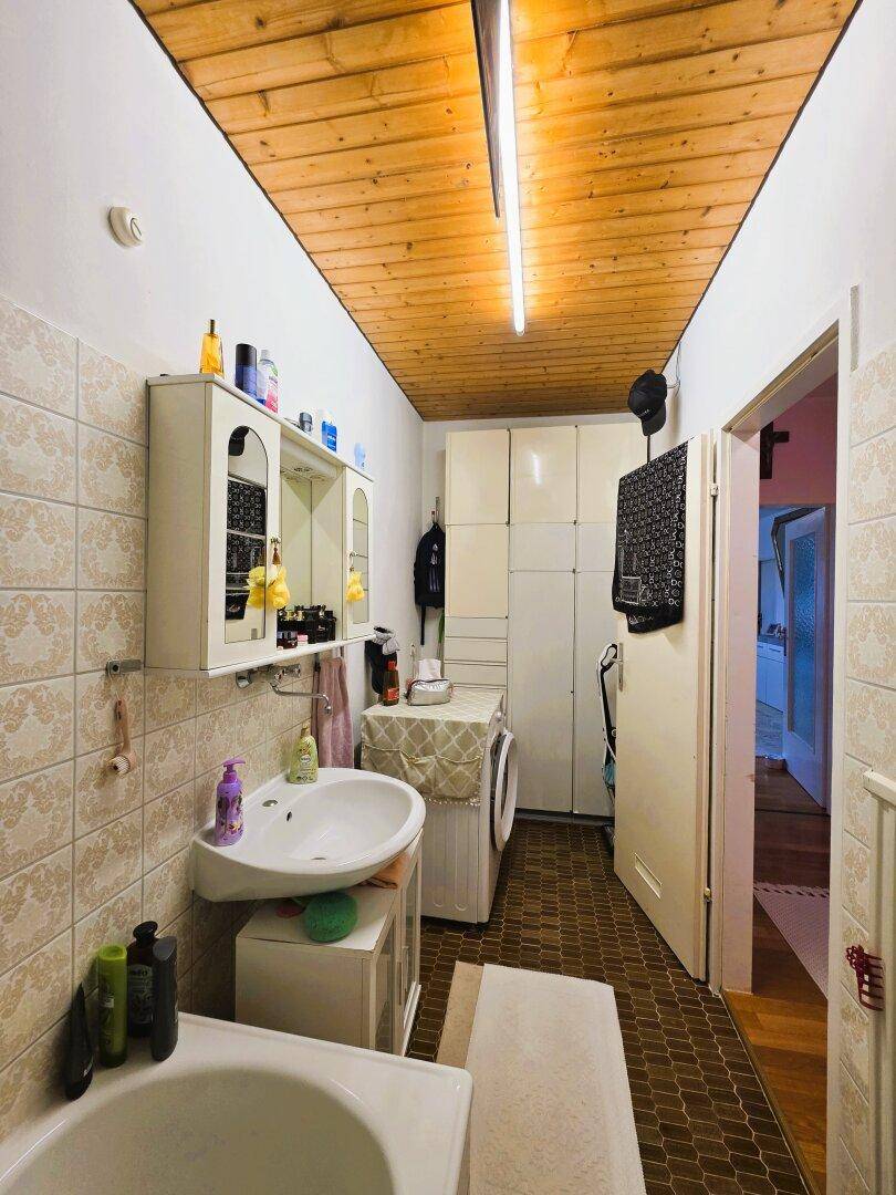 Langes Badezimmer mit Badewanne, Waschmaschine und Holzdecke.