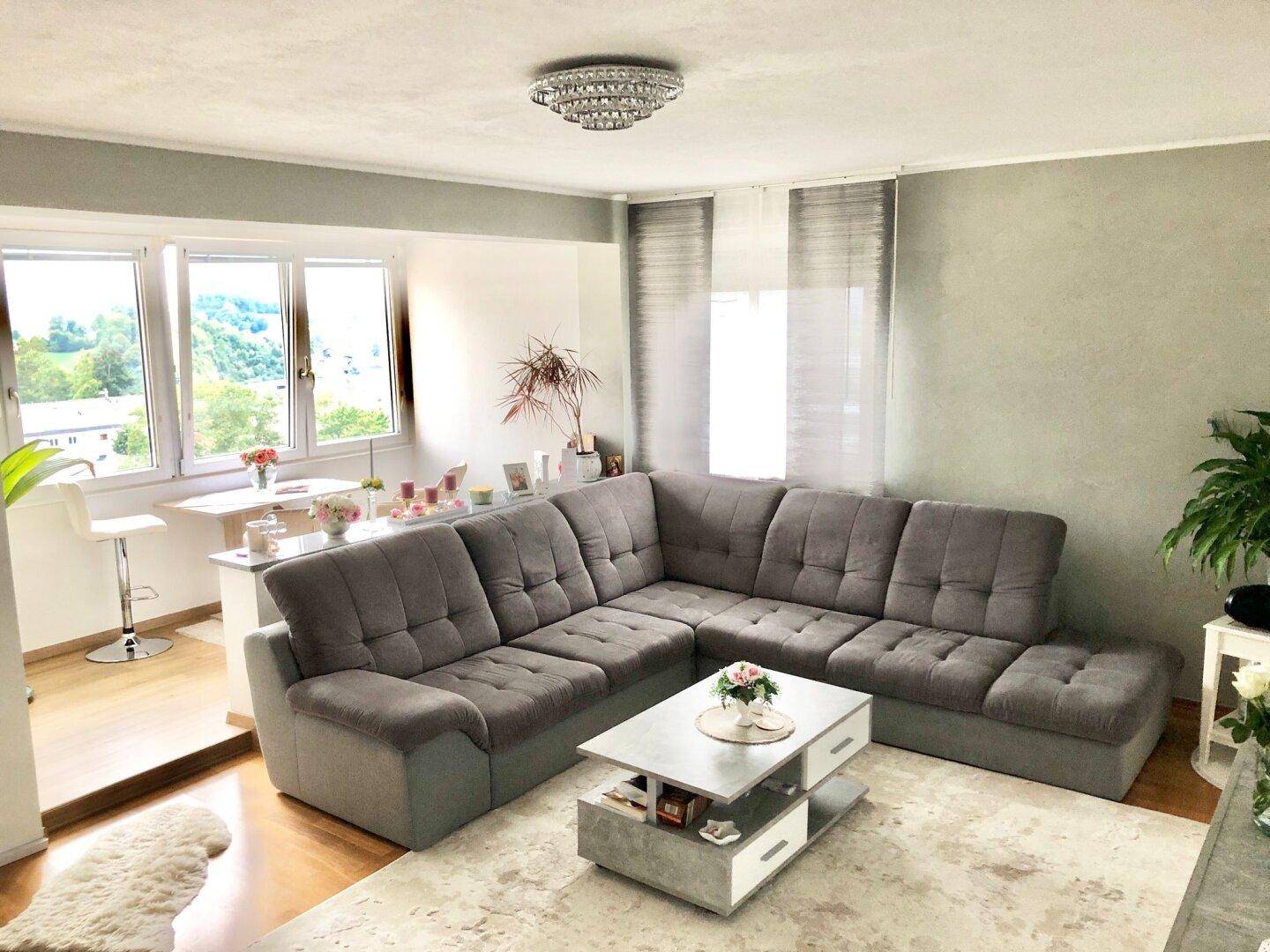 Geräumiges Wohnzimmer mit großem Ecksofa, Couchtisch und Essbereich am Fenster mit Bergblick.
