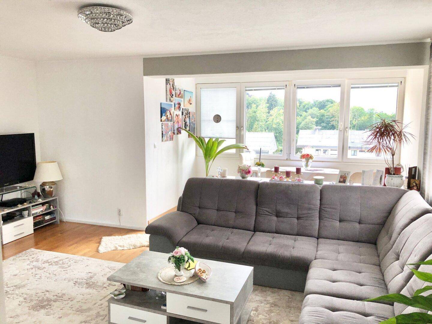 Helles Wohnzimmer mit bequemer Eckcouch, Fernseher und Essbereich am Fenster mit Blick ins Grüne.