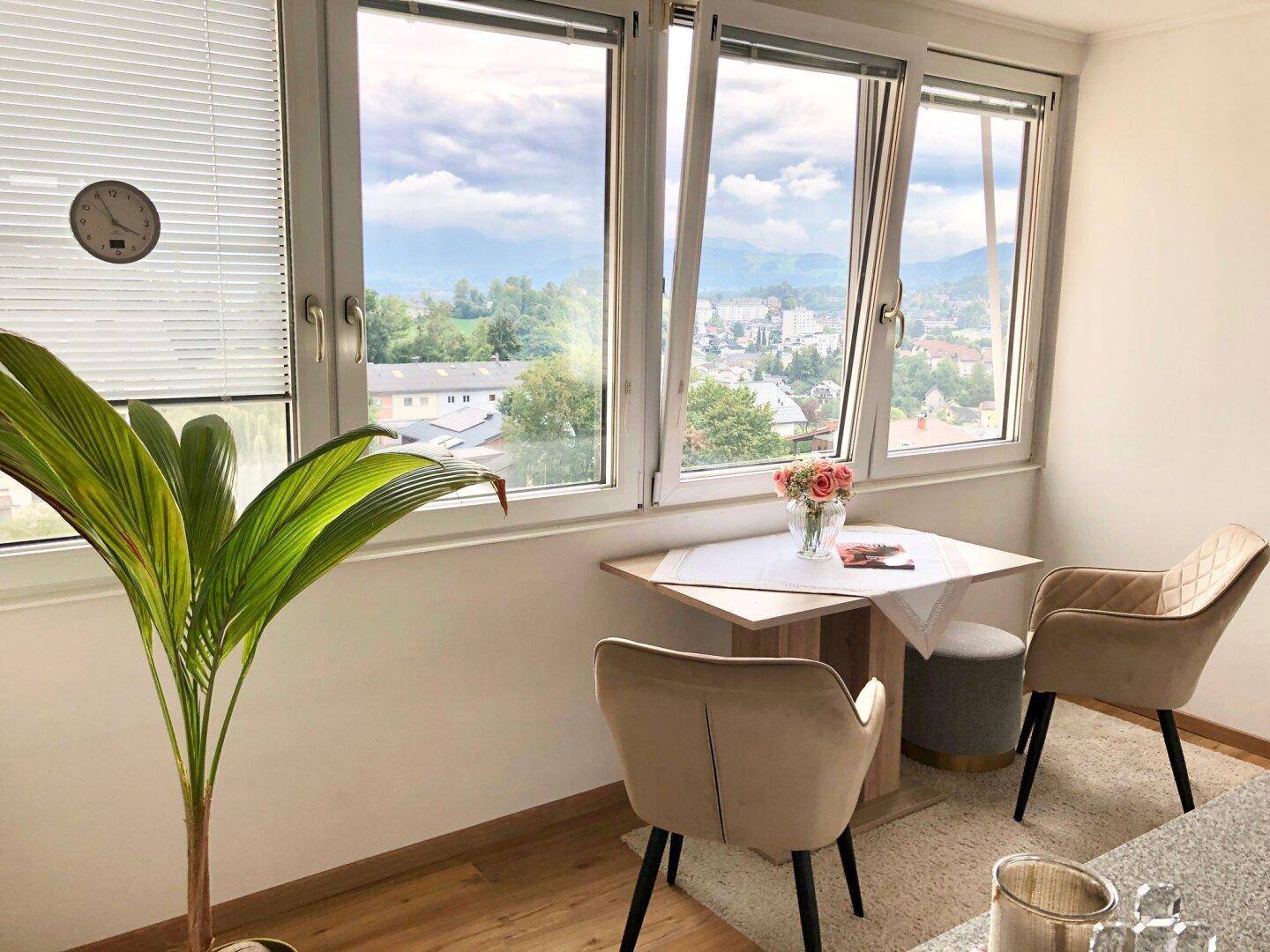 Kleiner Essbereich am Fenster mit zwei Stühlen und weitem Blick über die Stadt und Berge.