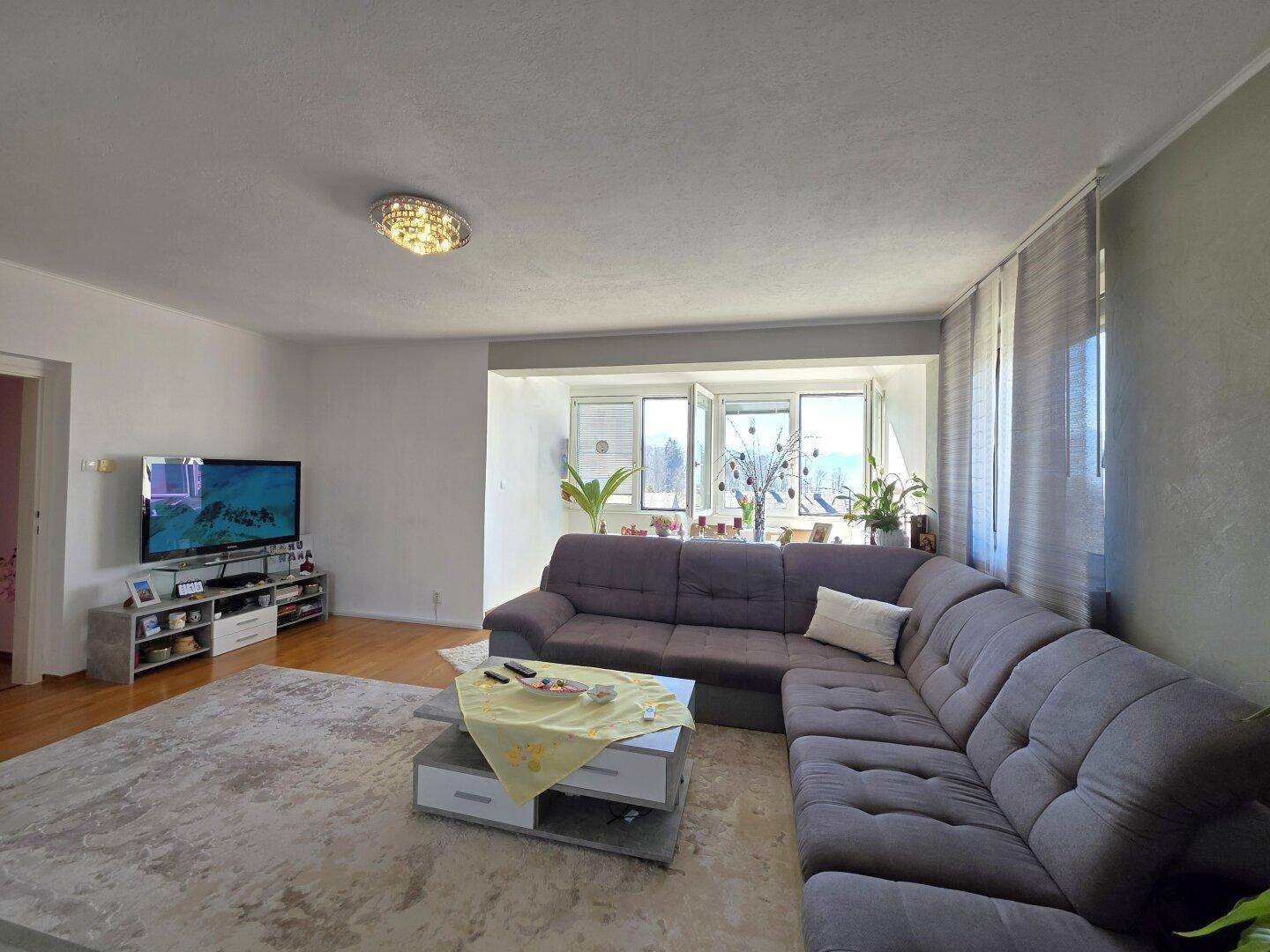 Gemütliches Wohnzimmer mit großem Ecksofa, Fernseher und Blick auf die umliegende Landschaft.