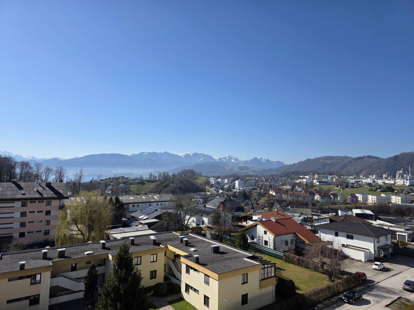 Weitläufiger Blick über die Stadt und die umliegende Landschaft mit majestätischen Bergen im Hintergrund.