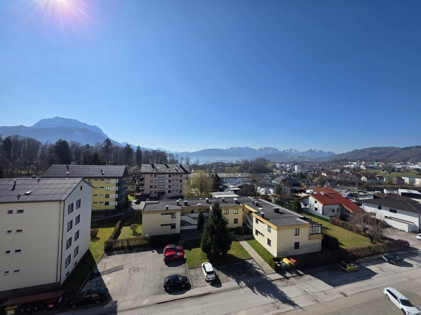 Panoramablick über die Wohngegend mit Gebäuden, Grünflächen und den Alpen im strahlenden Sonnenschein.