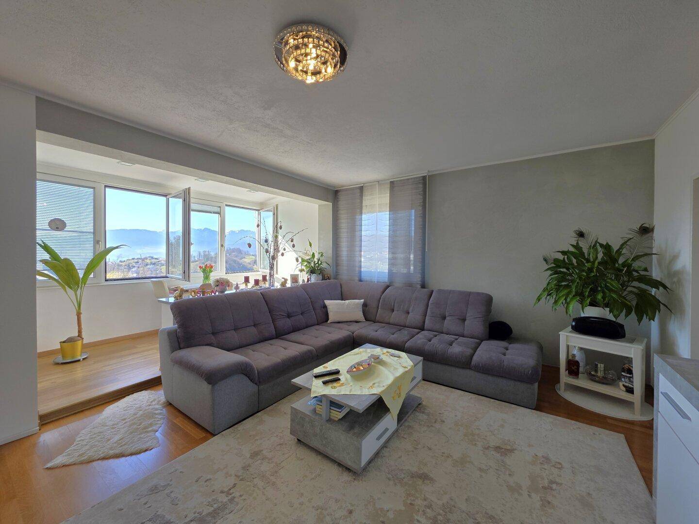 Geräumiges Wohnzimmer mit großem Ecksofa und Zugang zu einem hellen Essbereich mit Bergblick.