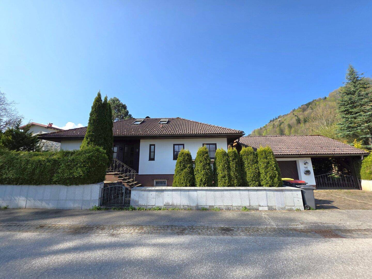 Vorderansicht des Hauses von der Straße aus, mit gepflegter Hecke, Garage und Carport im Hintergrund.