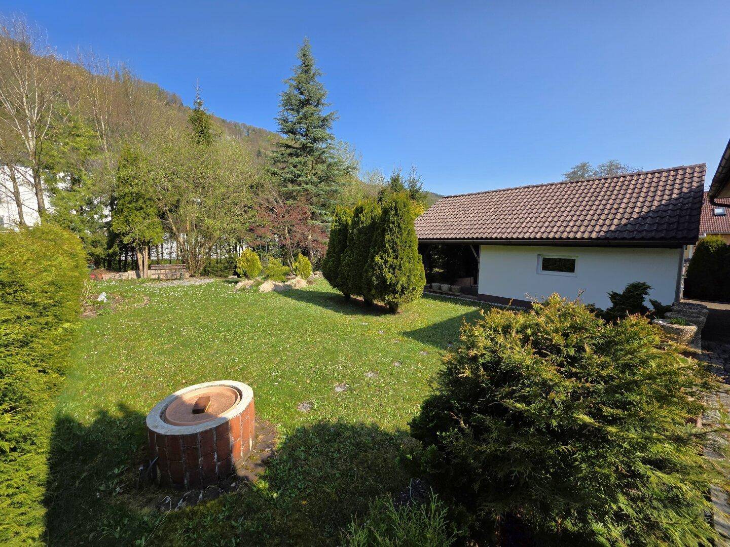 Gepflegter Gartenbereich mit Rasenfläche, Feuerstelle und Blick auf die umliegende Berglandschaft.